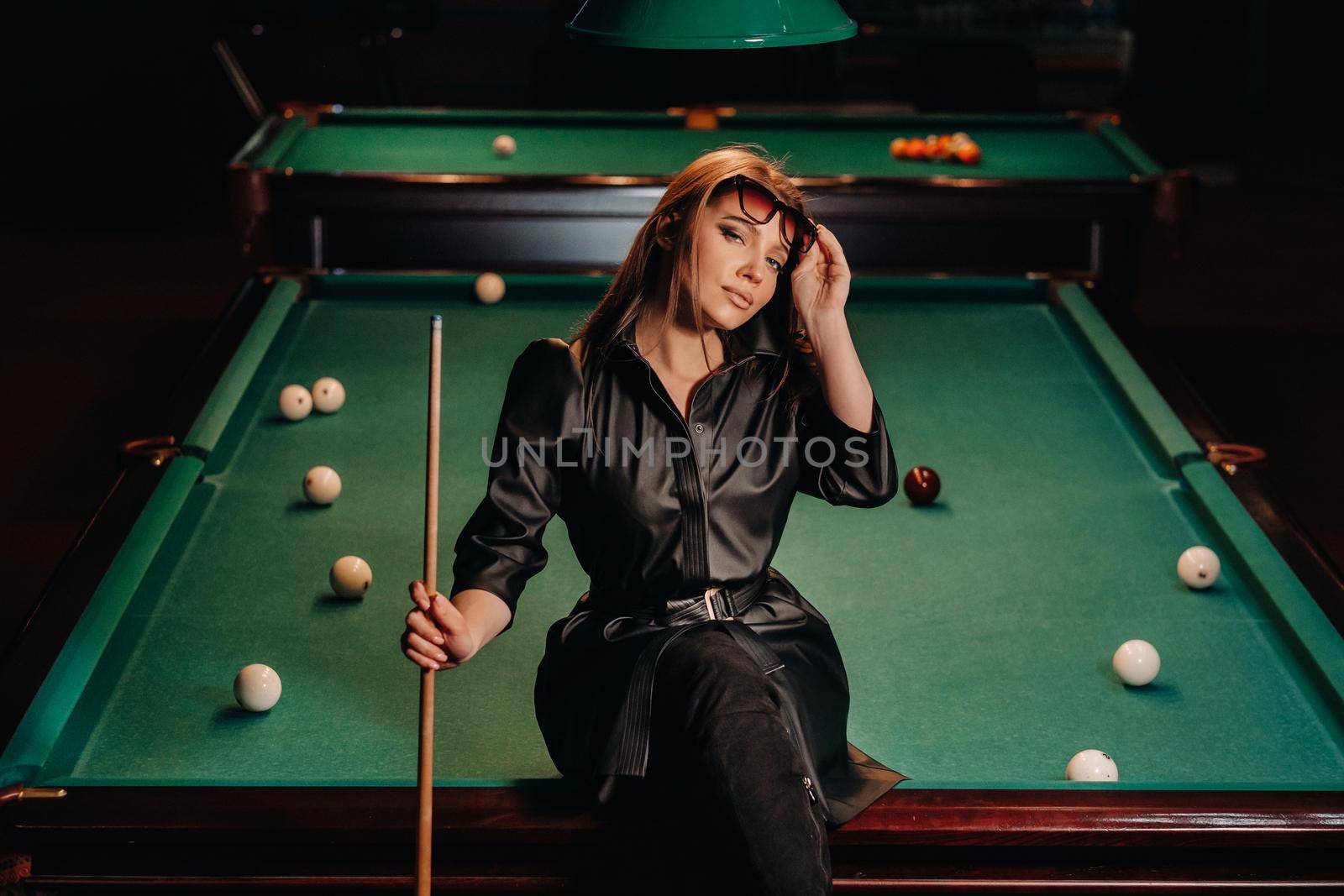A girl with glasses sits on a pool table in a club.Russian billiards.