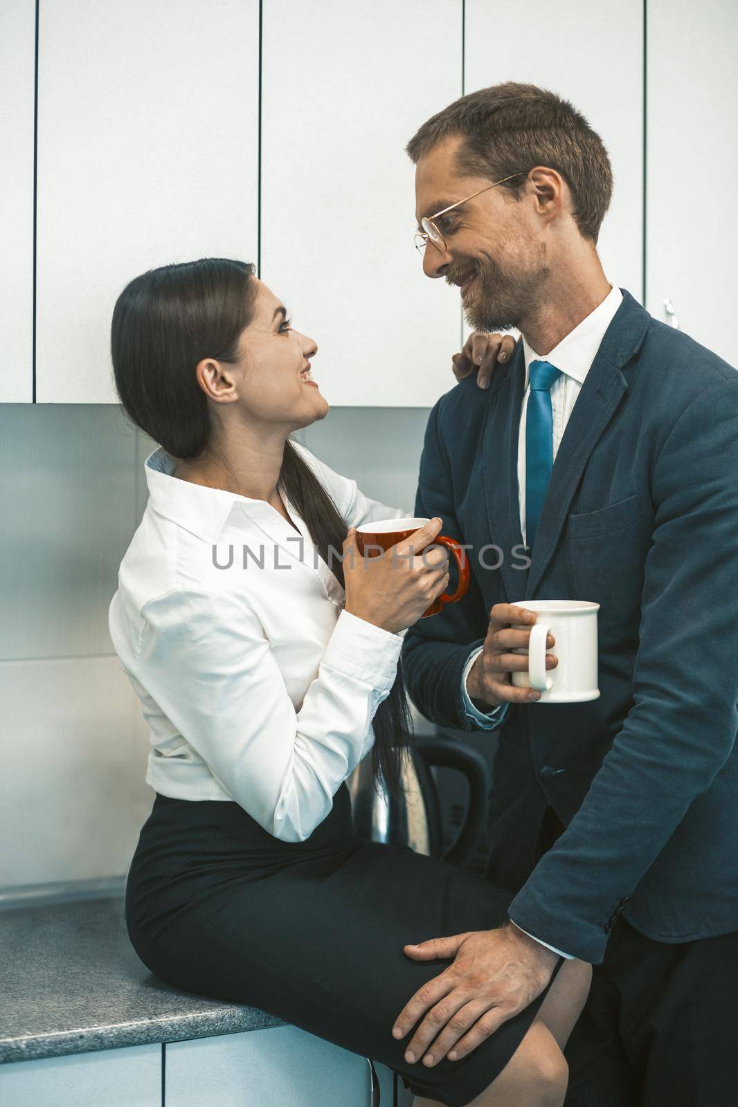 Couple drinking coffee and flirting during lunchtime. Smiling man and woman hold cups of hot drinks looking each other. Office romance concept. High quality photo.