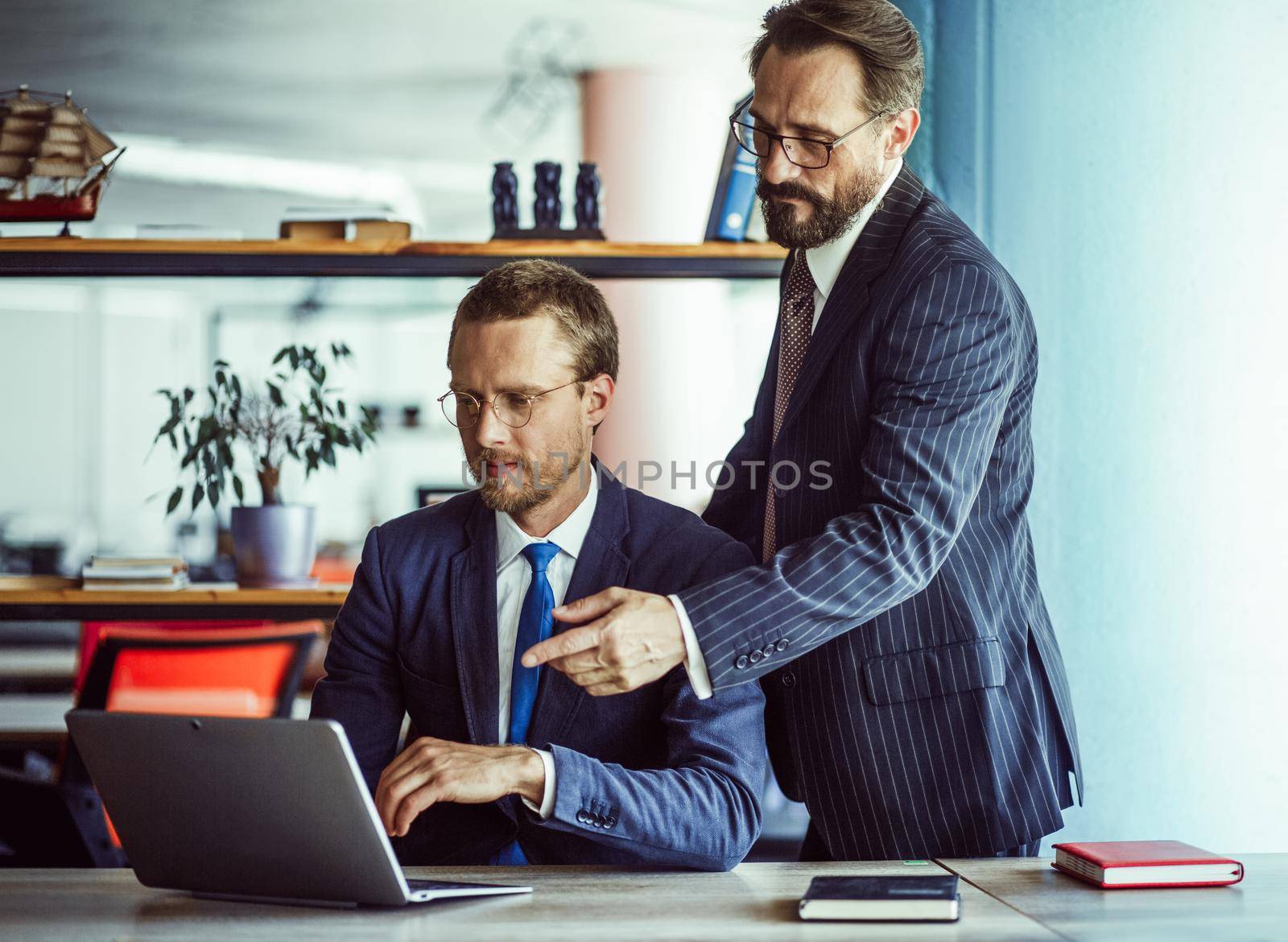 Two businessmen working with laptop in office. Male colleagues pointing and looking at computer screen. Teamwork concept. Toned image by LipikStockMedia