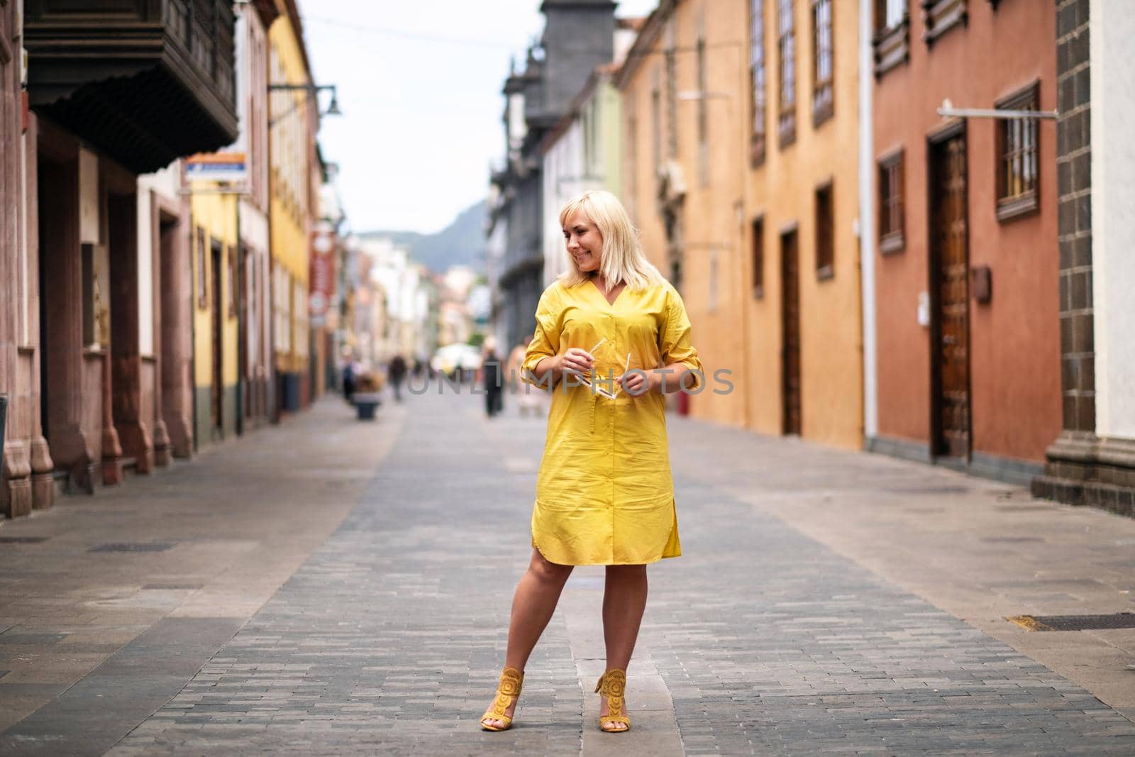 a blonde woman in a yellow summer dress stands on the street of the Old town of La Laguna on the island of Tenerife.Spain, Canary Islands.