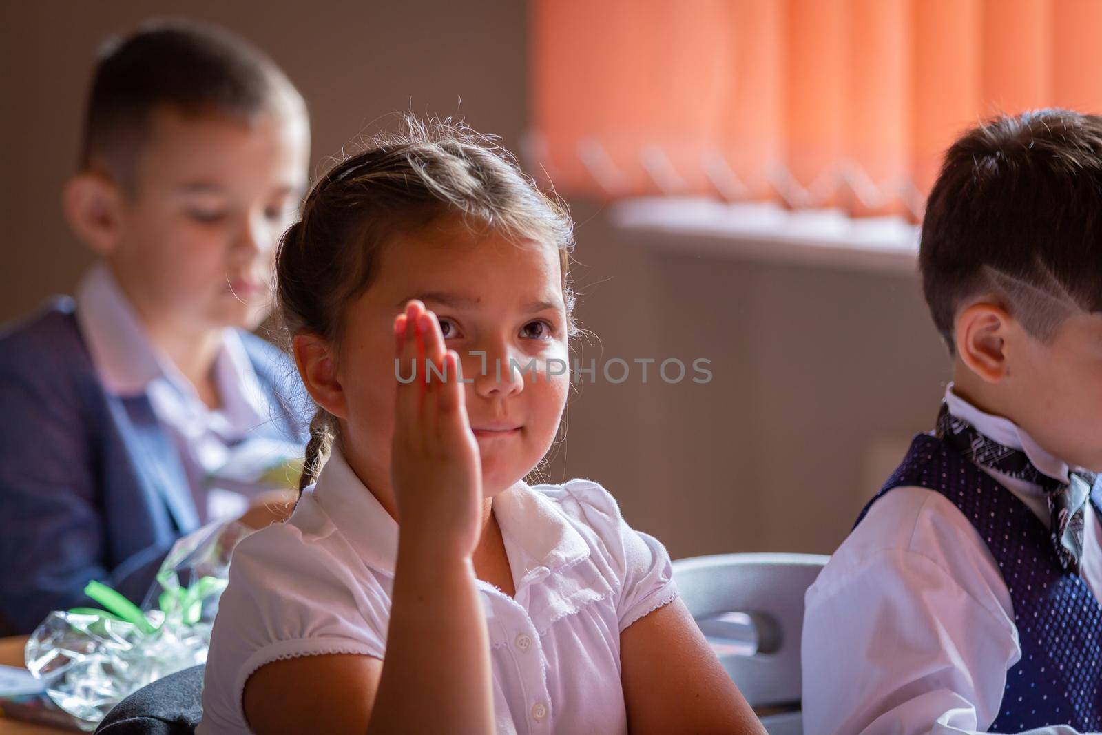The first grader sits at her desk with her hand raised, wants to answer the teacher. September 1. School. First grade. Moscow, Russia, September 2, 2019