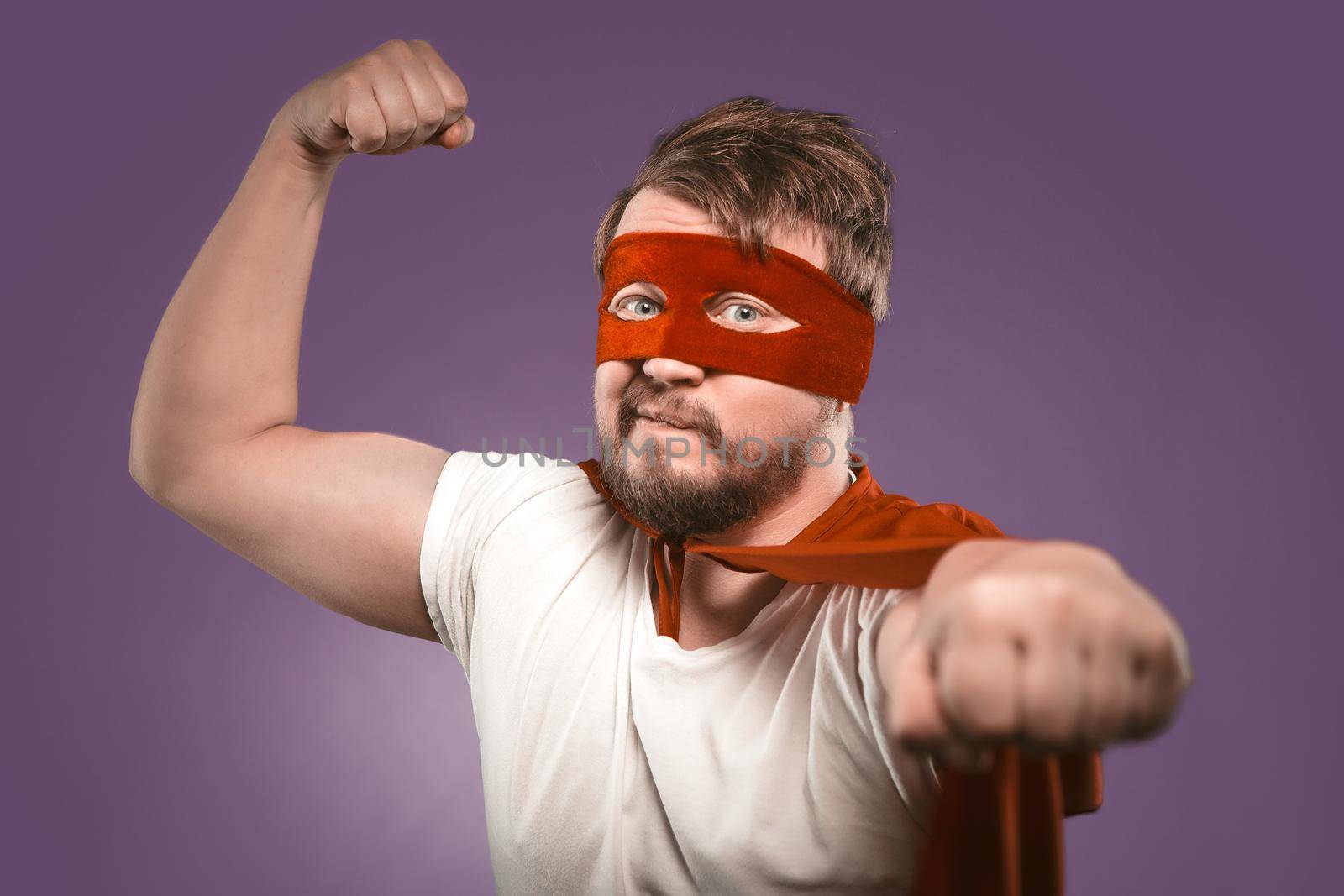 Super hero man shows muscles with fist forward looking at camera. Close up portrait. Selective focus on male face. Strong man on grape purple background.