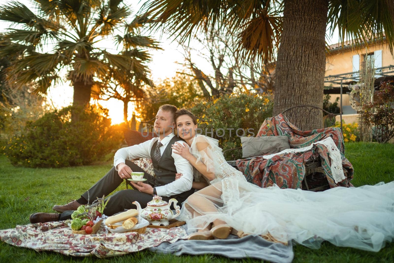 Newlyweds ' dinner on the lawn at sunset.A couple sits and drinks tea at sunset in France by Lobachad
