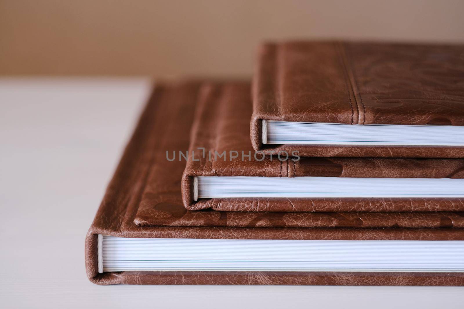 Composition of photo books in natural brown leather of different sizes. Fragment of a photobook binding.