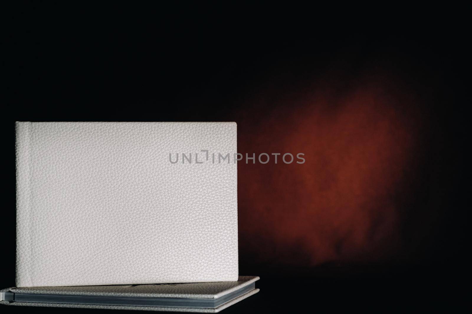 Composition of photo books in natural white leather of different sizes. The white paper on a dark background