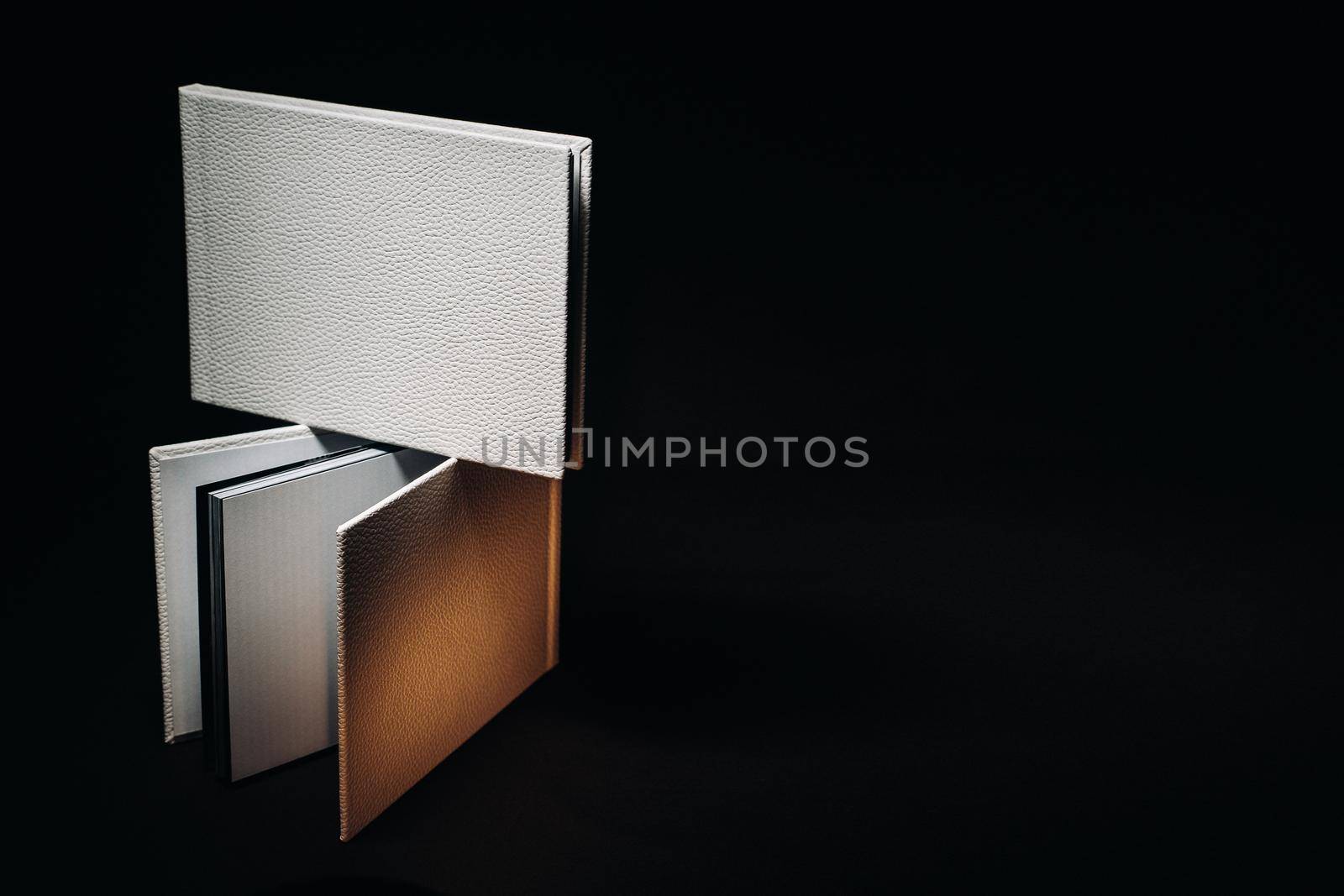 Composition of photo books in natural white leather of different sizes. The white paper on a dark background
