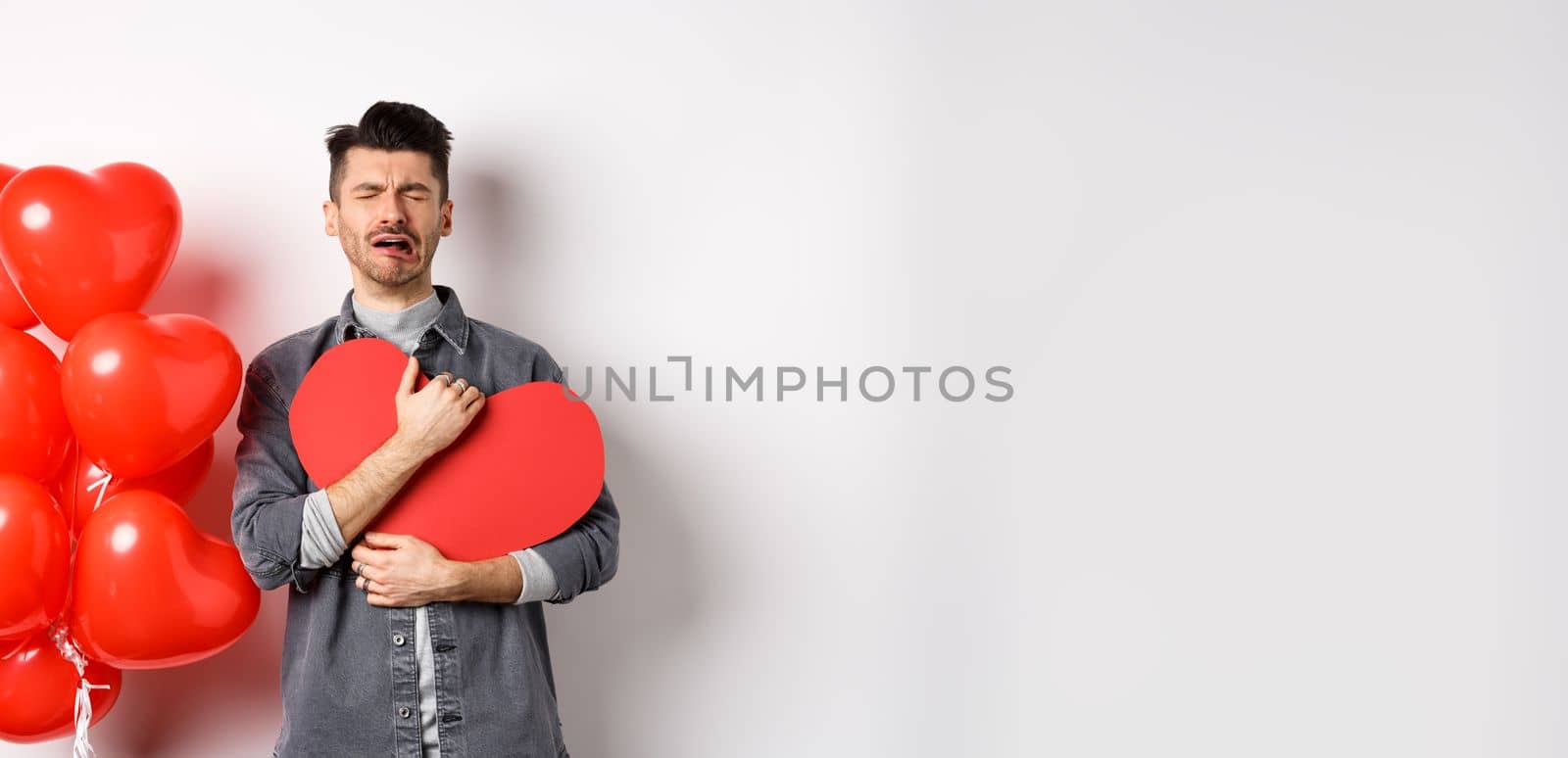 Crying man standing single and lonely on Valentines day, hugging heart cutout and sobbing miserable, being heartbroken and rejected by lover, white background by Benzoix