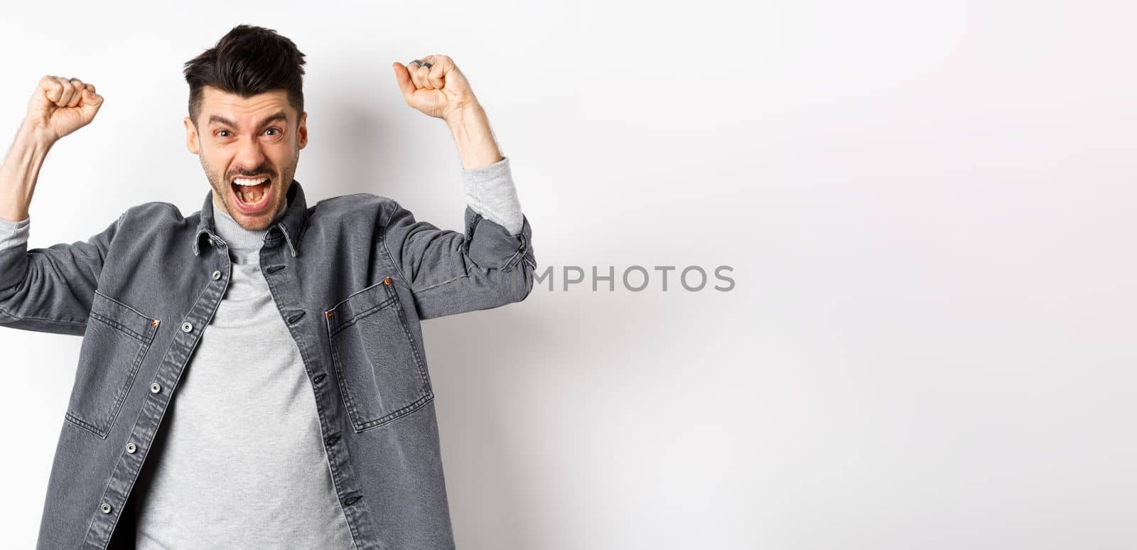 Motivated young man shouting and raising hands up, watching sports game and rooting for team, cheering and chanting, standing on white background by Benzoix