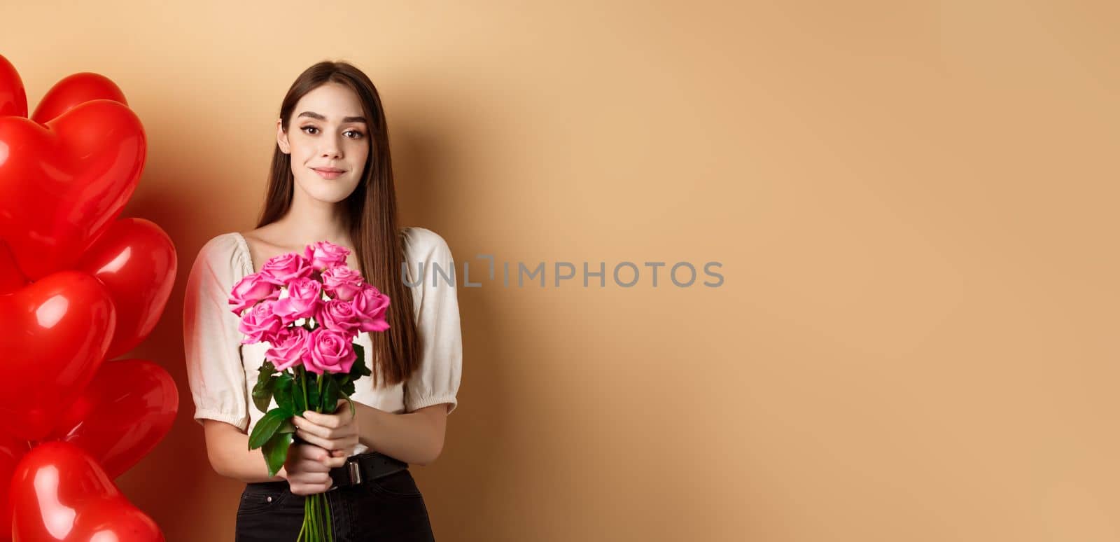 Beautiful girl holding bouquet of pink roses and smiling at camera, going on romantic date, standing near valentines heart balloons, beige background by Benzoix