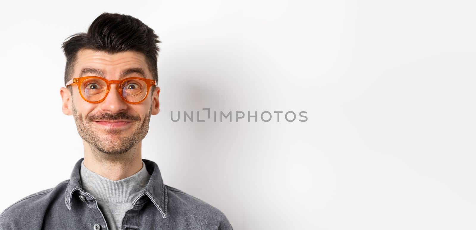 Close-up of happy man with moustache and glasses looking at camera, smiling pleased, standing against white background.