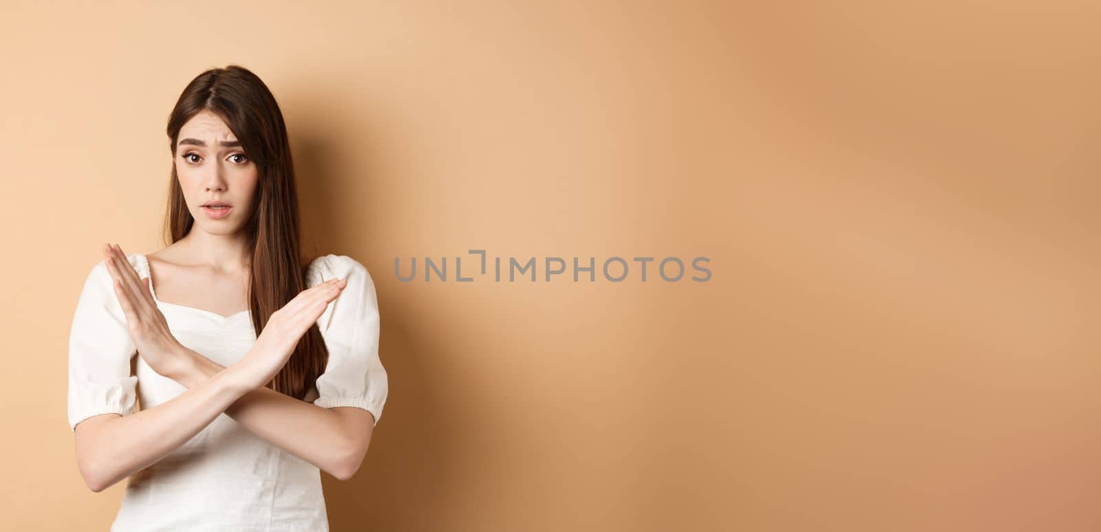 Girl says no. Skeptical young woman disagree or prohibit action, showing cross stop gesture, make nope sign, disapprove bad idea, standing on beige background by Benzoix