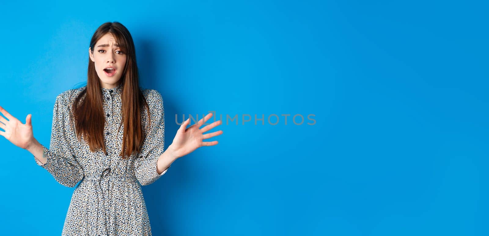 Sad and gloomy woman in dress facing failure, looking distressed and sighing upset, losing and standing on blue background.
