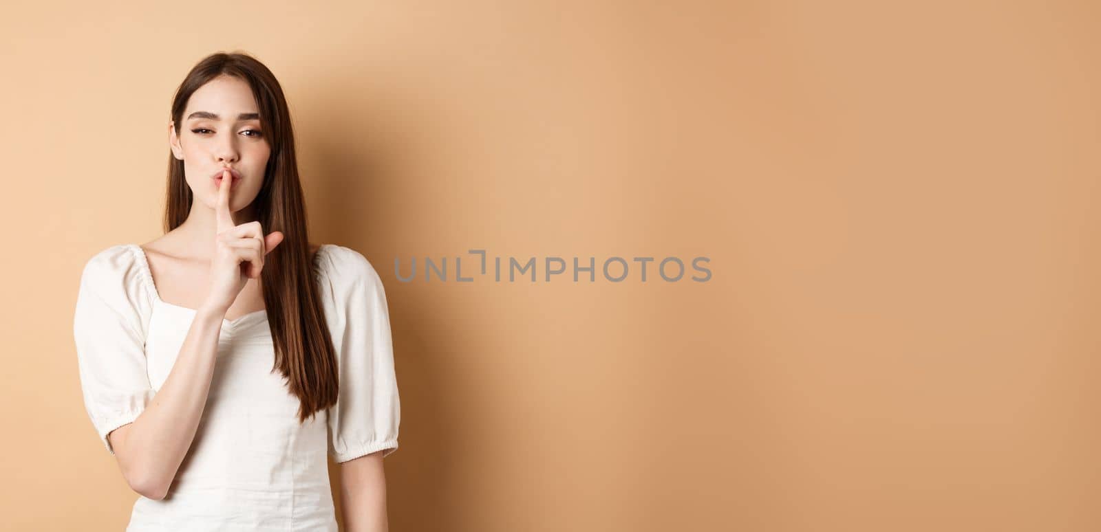 Sensual cute girl hiding secret, showing hush gesture, make shhh sound with finger on lips, stay quiet sign, standing on beige background by Benzoix
