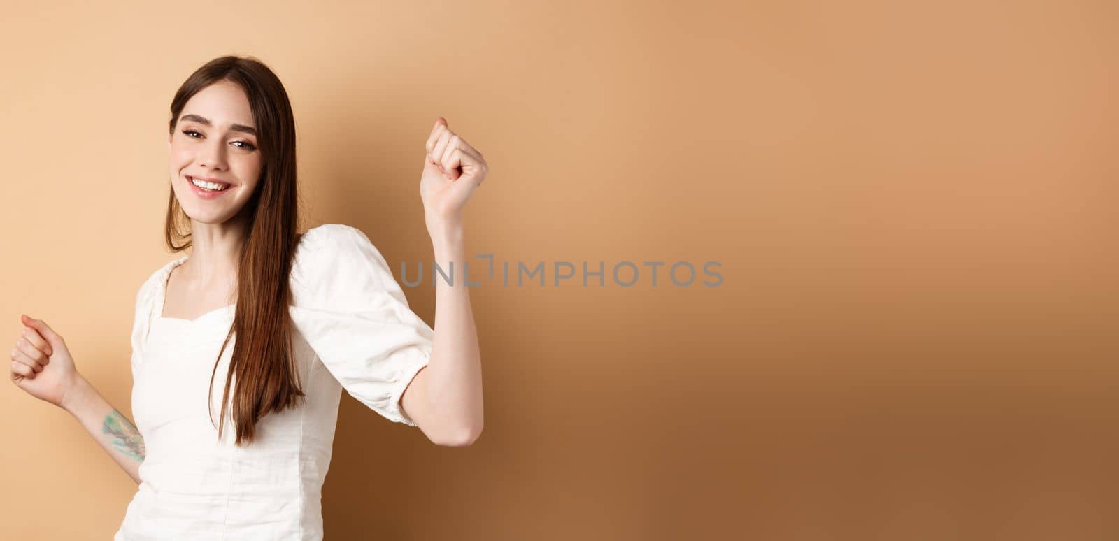 Happy woman dancing and having fun, close eyes and smiling, standing on beige background by Benzoix