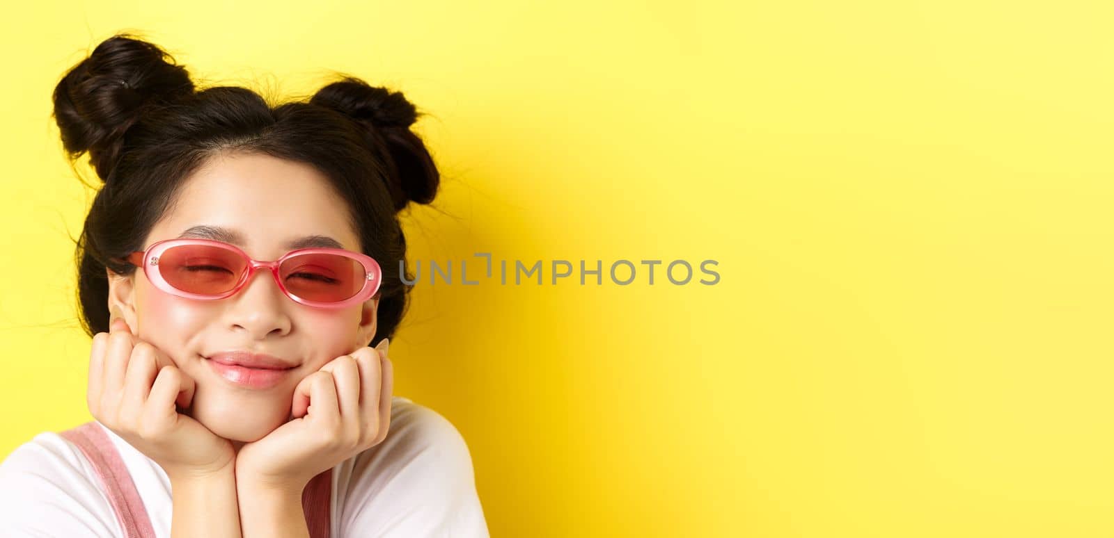 Summer fashion concept. Dreamy asian girl with romantic face expression, daydreaming or imaging something beautiful with closed eyes and happy smile, wearing sunglasses.