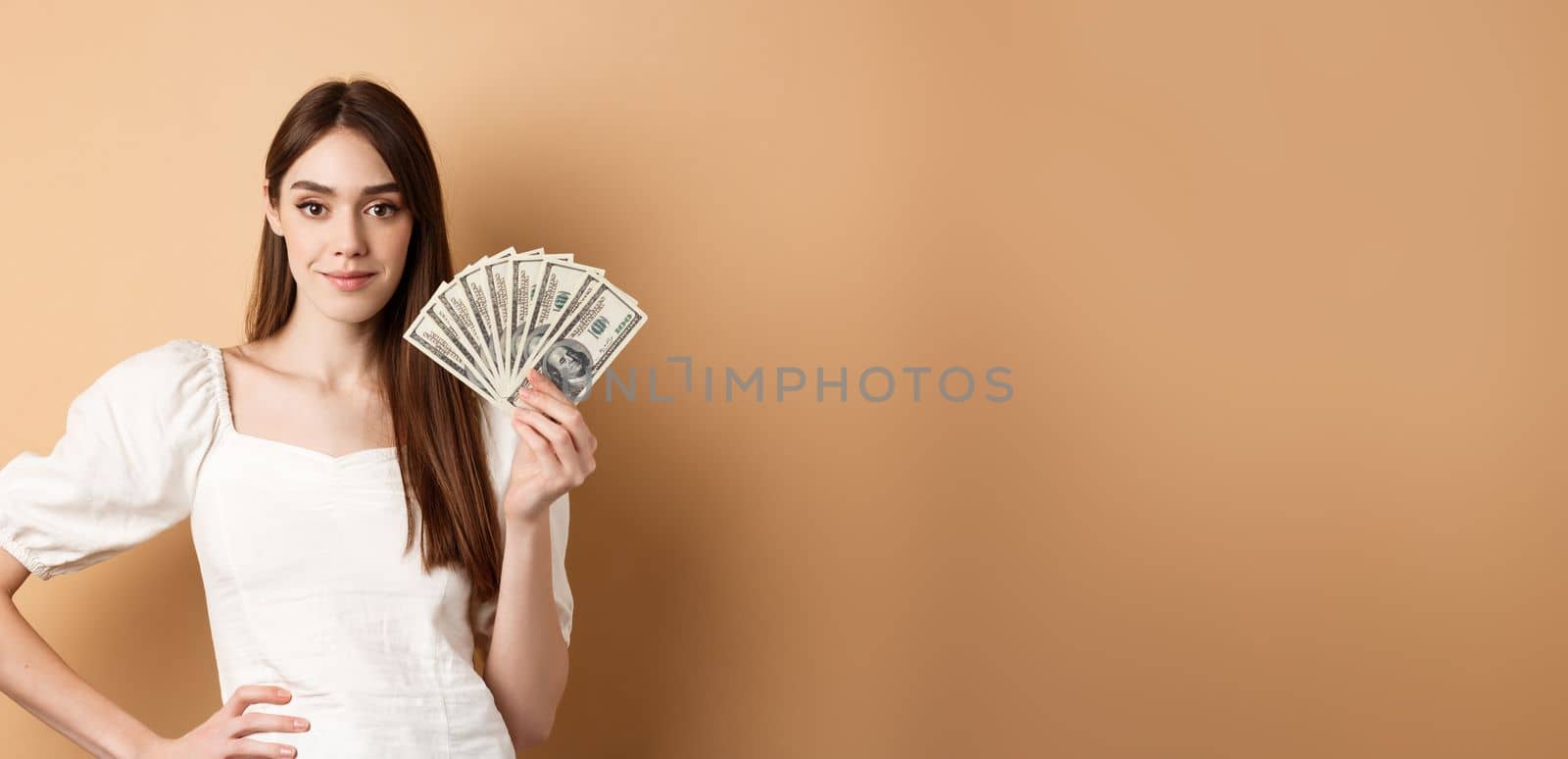 Confident smiling woman showing dollar bills, earn money and look satisfied, standing on beige background with cash by Benzoix