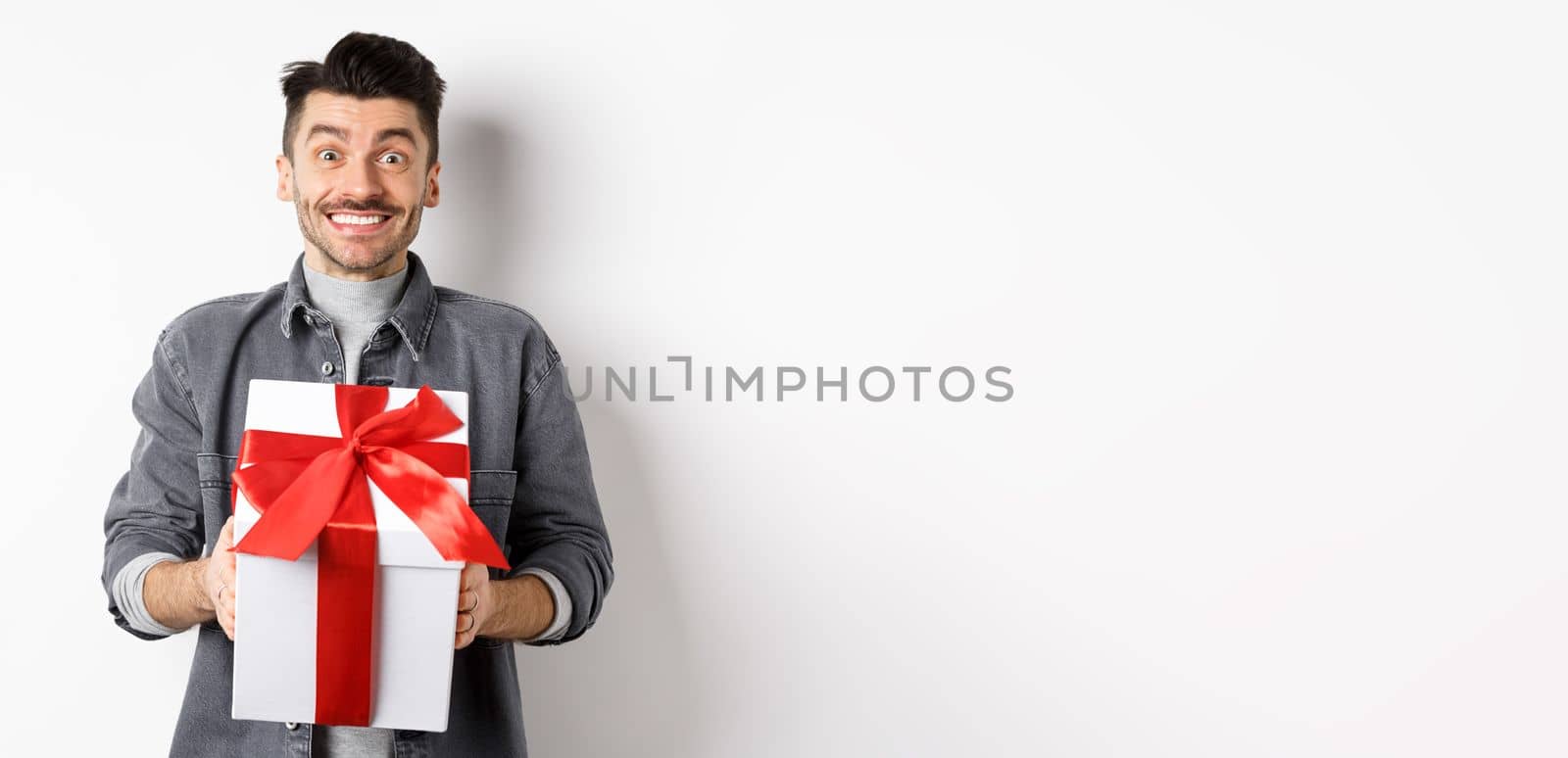 Cheerful caucasian guy holding surprise gift, receive present on holiday and smiling thankful, looking grateful at camera, celebrating Valentines day, white background by Benzoix