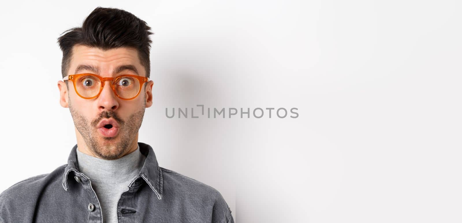 Wow look there. Excited handsome man in stylish glasses stare impressed at camera, checking out eyewear store offer, standing on white background.