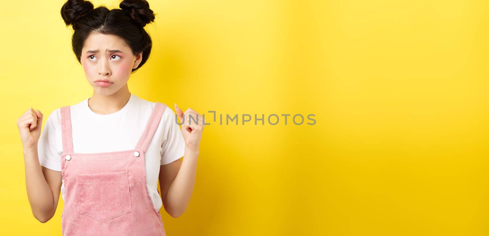 Timid angry girl sulking and clenching teeth, feeling mad but looking cute at upper left corner, standing with makeup on yellow background by Benzoix