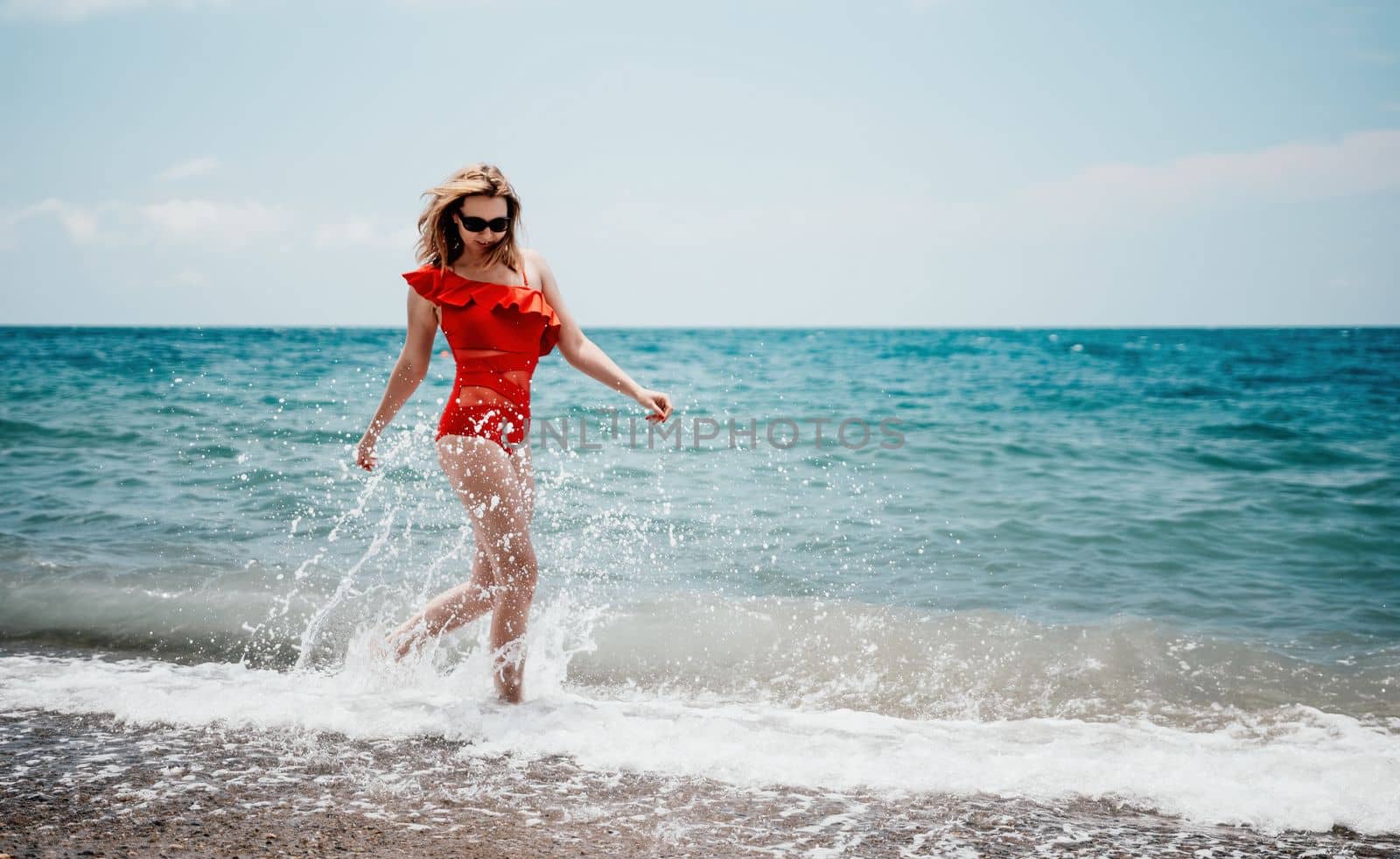 Young happy woman walks carefree on the seaside. Happy lady in red bikini. Portrait beautiful young woman relax smile around beach sea ocean in holiday vacation travel trip.