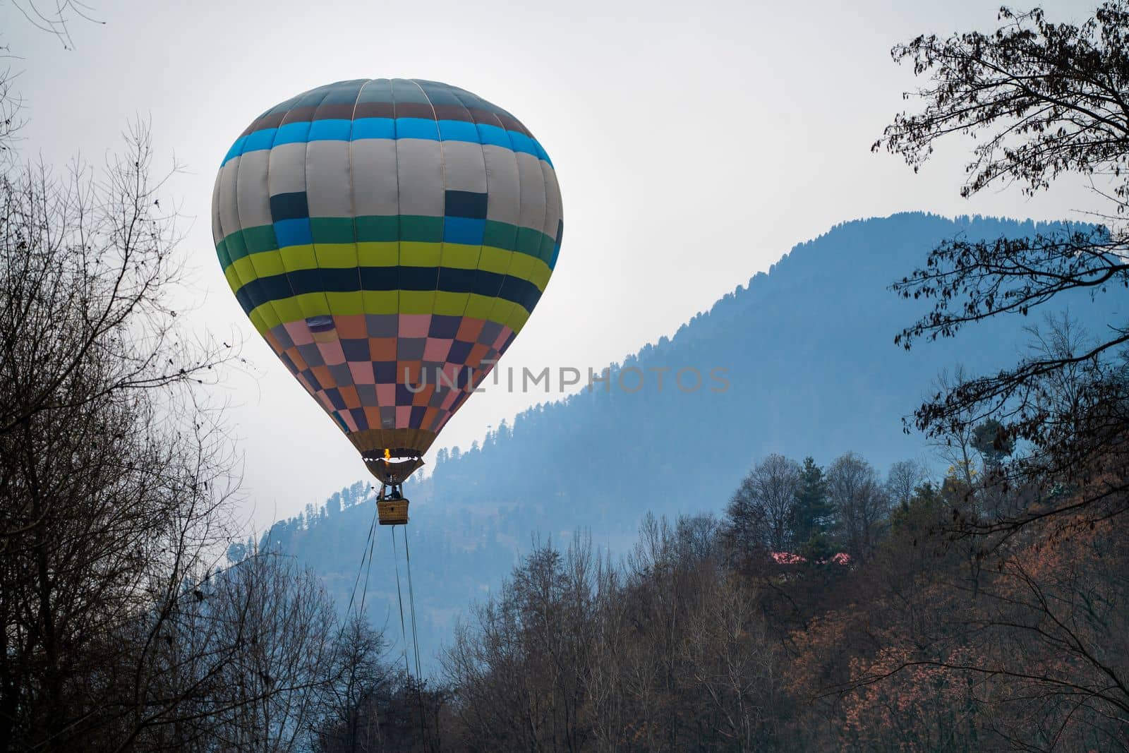 Hot air balloon with fire heating air in wicker basket with himalaya mountains in background showing this adventure in kullu manali valley India
