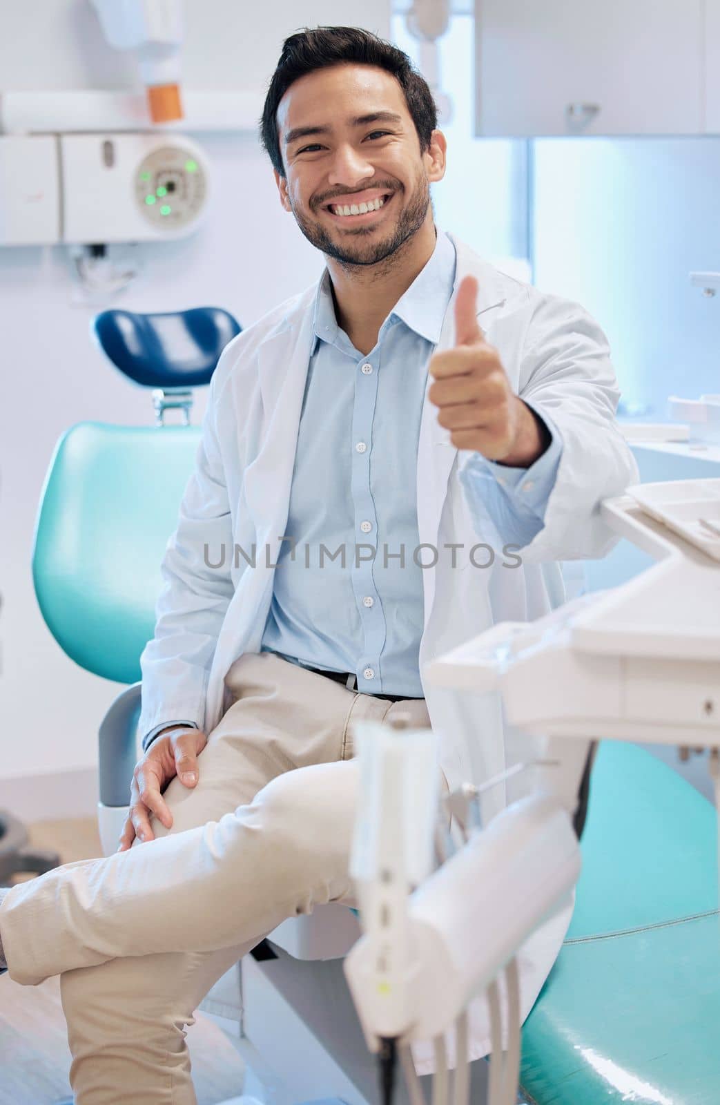 Im here to do my best. a young male dentists giving the thumbs up in his office. by YuriArcurs