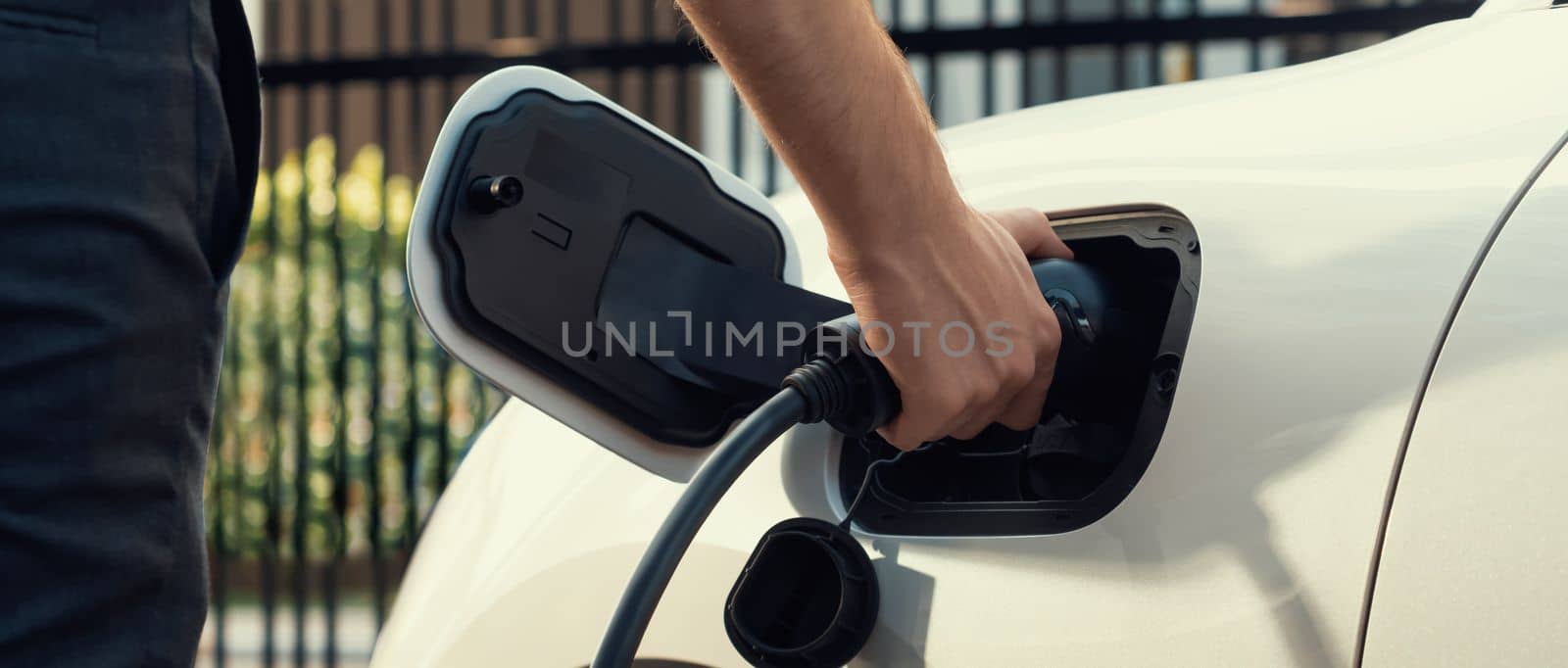 Closeup progressive man holding EV charger plug from public charging station for electric vehicle with background of residential building as concept eco-friendly sustainability energy car concept.