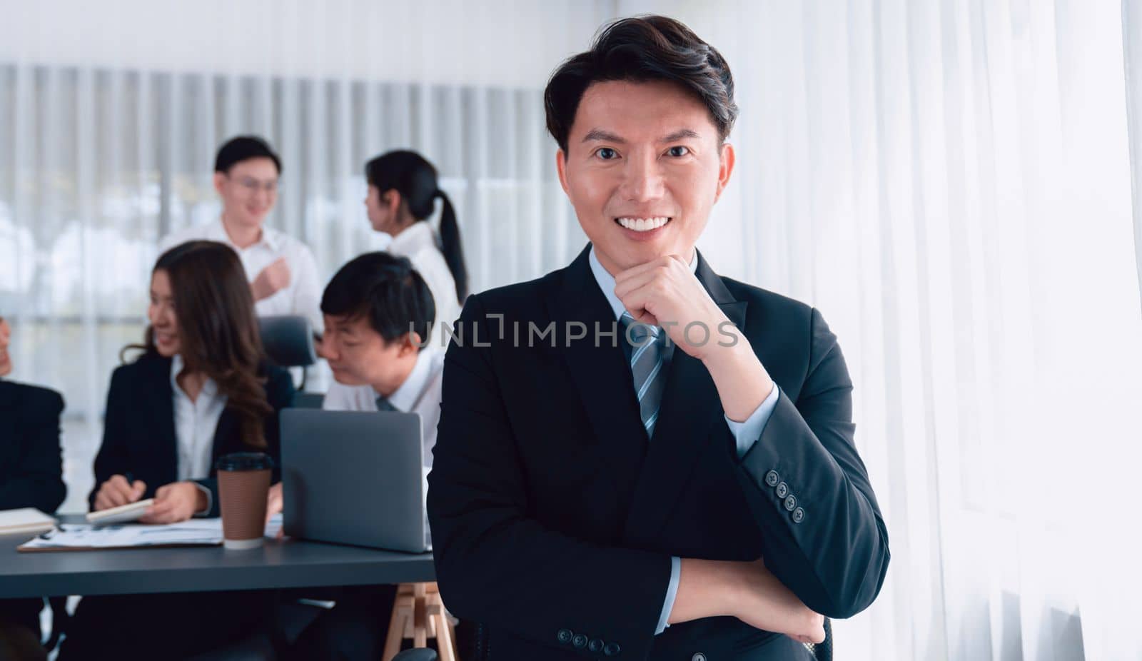 Portrait of focus young successful confident male manager, executive wearing business wear in harmony office arm crossed with blurred meeting background of colleagues, office worker.