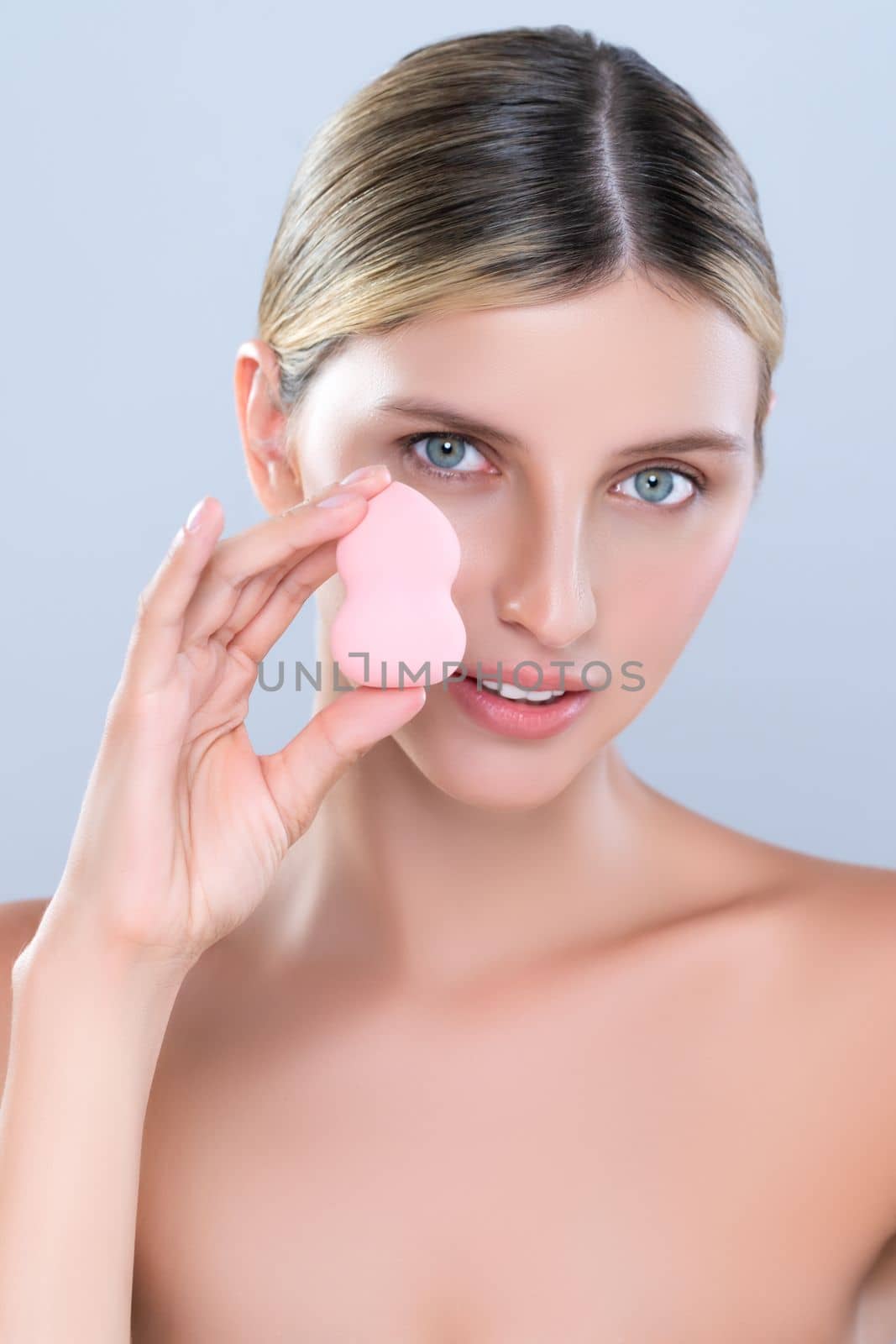 Alluring beautiful female model applying powder puff for facial makeup concept. Portrait of flawless perfect cosmetic skin woman put powder foundation on her face in isolated background.