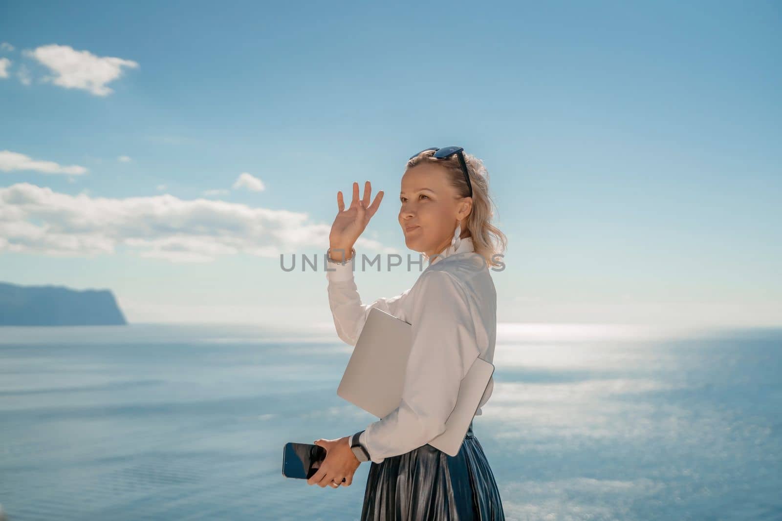 Freelance women sea working on a computer. Pretty middle aged woman with computer and phone outdoors with beautiful sea view. The concept of remote work