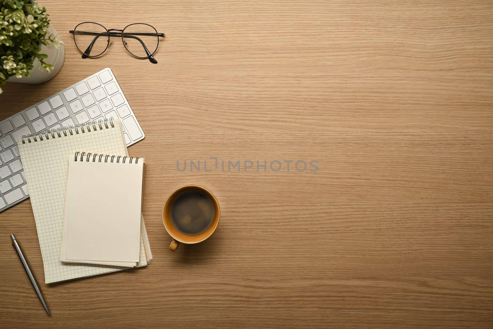 Simple workplace with notebooks, eyeglasses, keyboard and coffee cup on wooden desk.