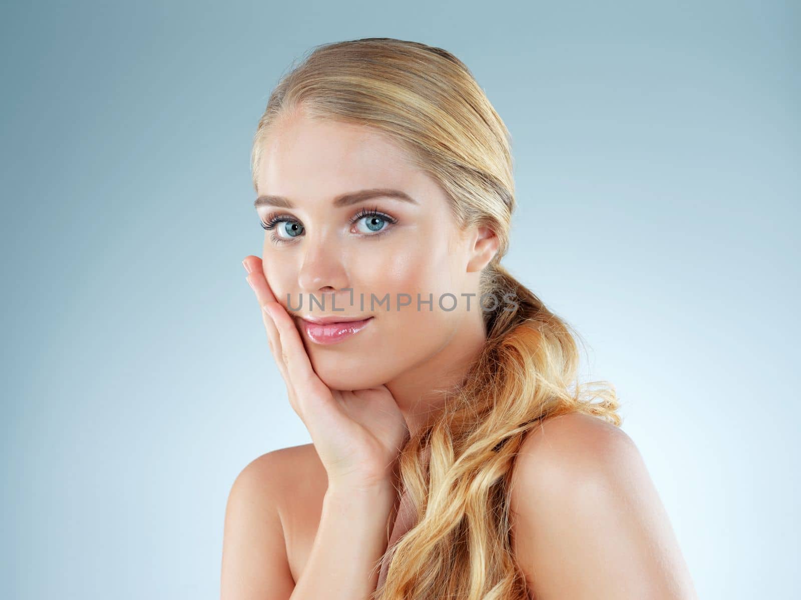 My skin feels amazing. Studio portrait of a beautiful young blonde woman posing against a blue background. by YuriArcurs