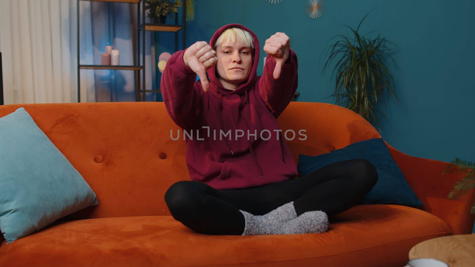 Dislike. Upset woman with short hair showing thumbs down sign gesture, expressing discontent, disapproval dissatisfied bad work at modern home apartment indoors. Displeased girl in living room on sofa