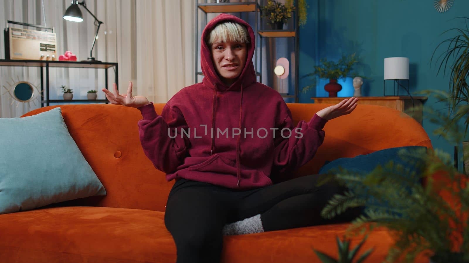 What. Why. Woman with short hair raising hands in indignant expression asking reason of failure demonstrating disbelief irritation by troubles at home apartment. Girl in evening room sitting on sofa