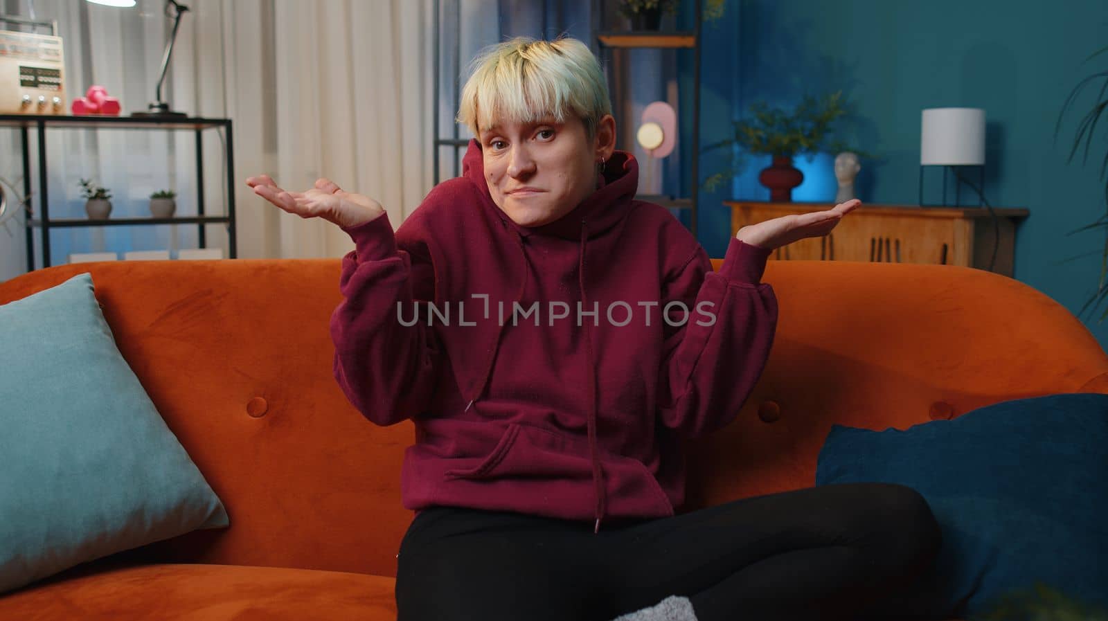 I dont know what to say. Confused young woman feeling embarrassed about ambiguous question, having doubts, no idea, being clueless uncertain at home. Girl at night living room. Lgbt gay lesbian people
