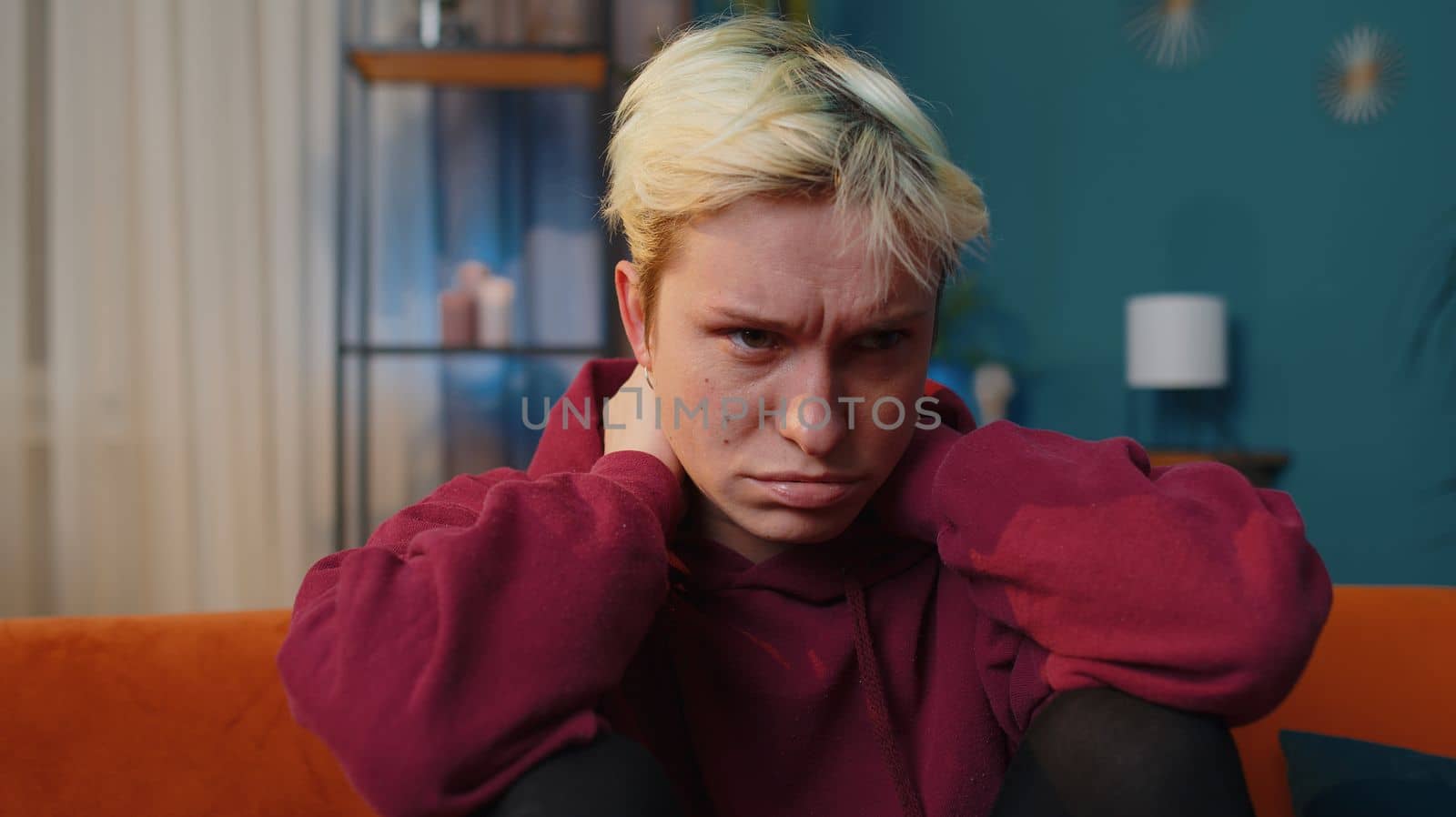 Displeased blonde woman rubbing temples to cure headache problem, suffering from tension and migraine, stress, grimacing in pain, high blood pressure. Girl at home in evening room sitting on couch