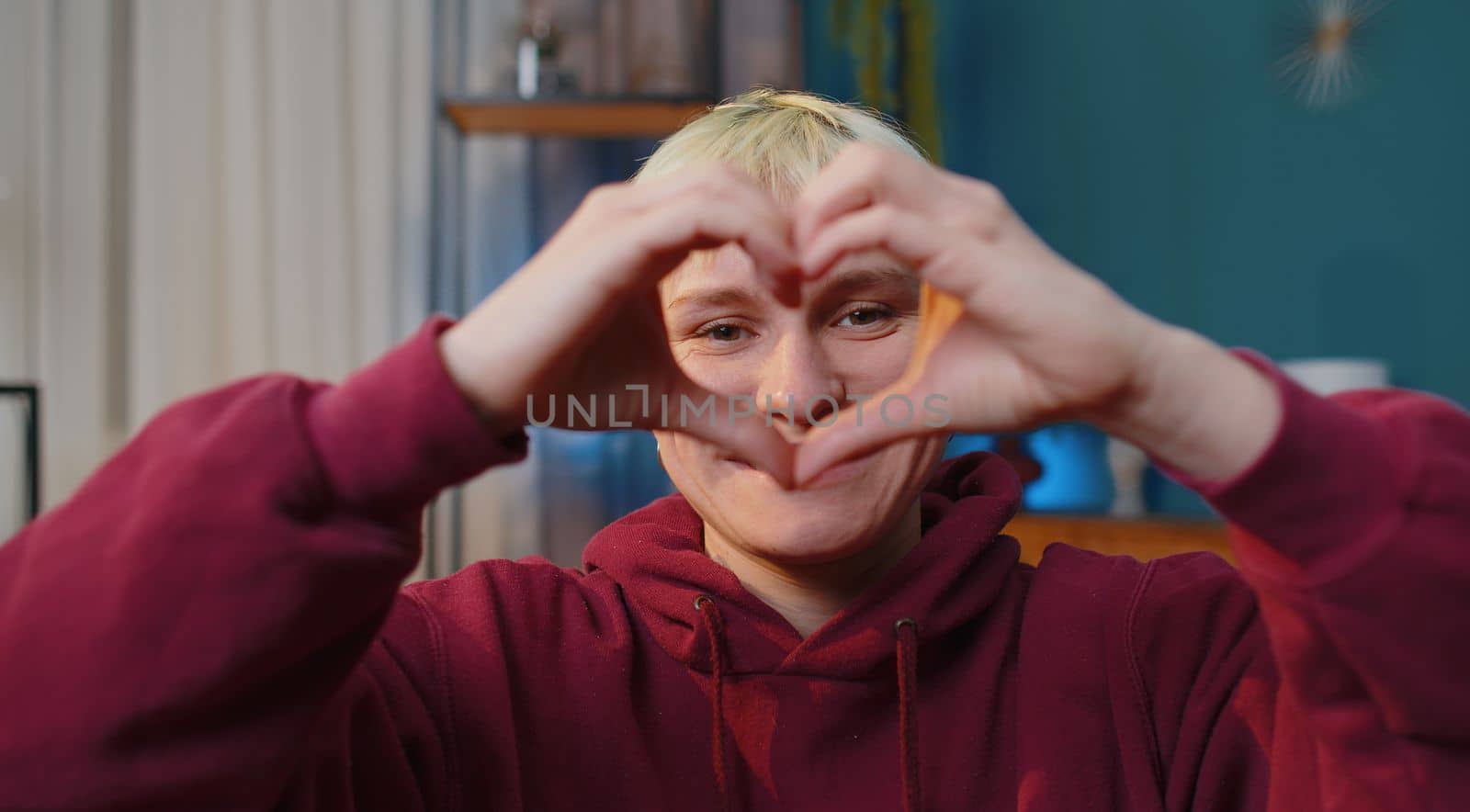I love you. Happy woman with short hair at home couch makes symbol of love, showing heart sign to camera, express romantic feelings express sincere positive feelings. Charity, gratitude, donation