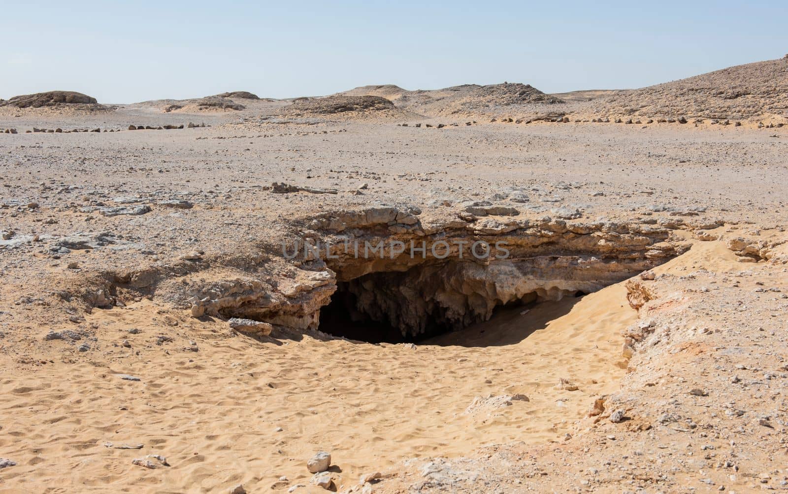 Barren rocky desert landscape in hot climate with cave entrance by paulvinten