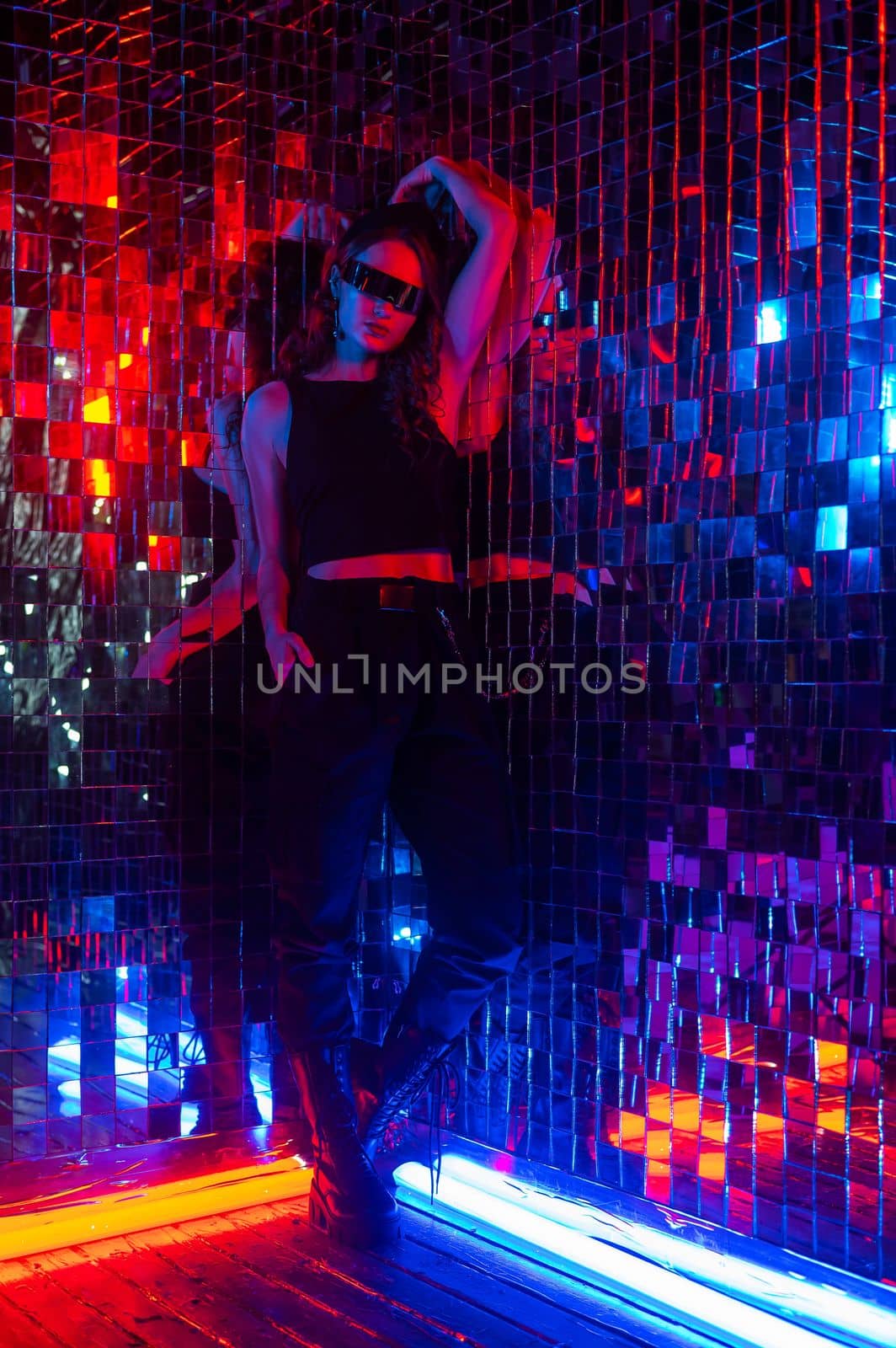 Portrait of a caucasian woman in sunglasses in neon light against a mirror wall