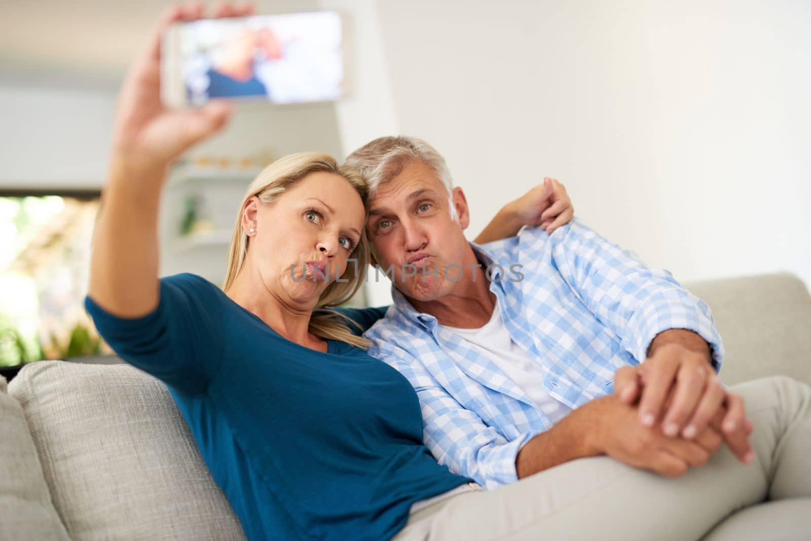 Is this how youre supposed to pose. a mature couple taking a selfie together at home. by YuriArcurs