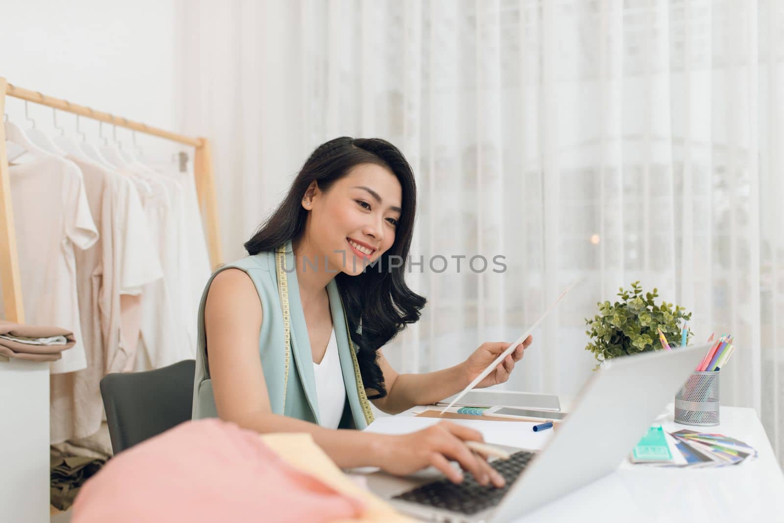 Fashion designer at work. Happy young Asian woman drawing while sitting at her working place in fashion workshop