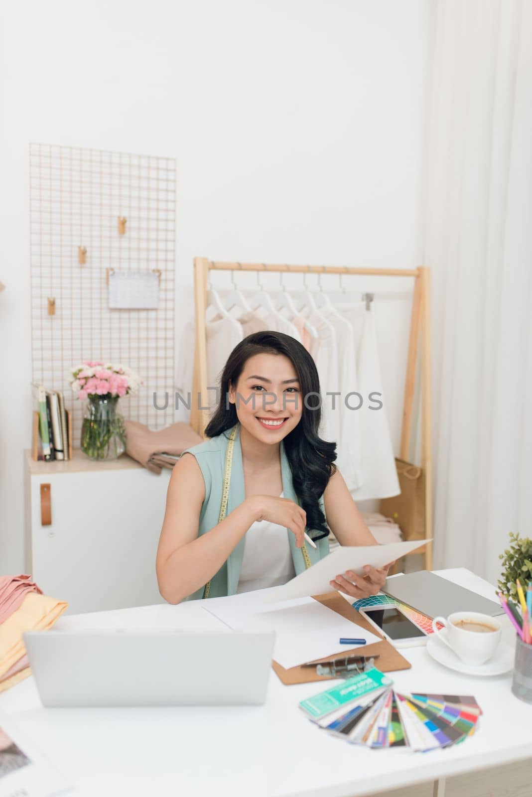 Fashion designer at work. Happy young Asian woman drawing while sitting at her working place in fashion workshop