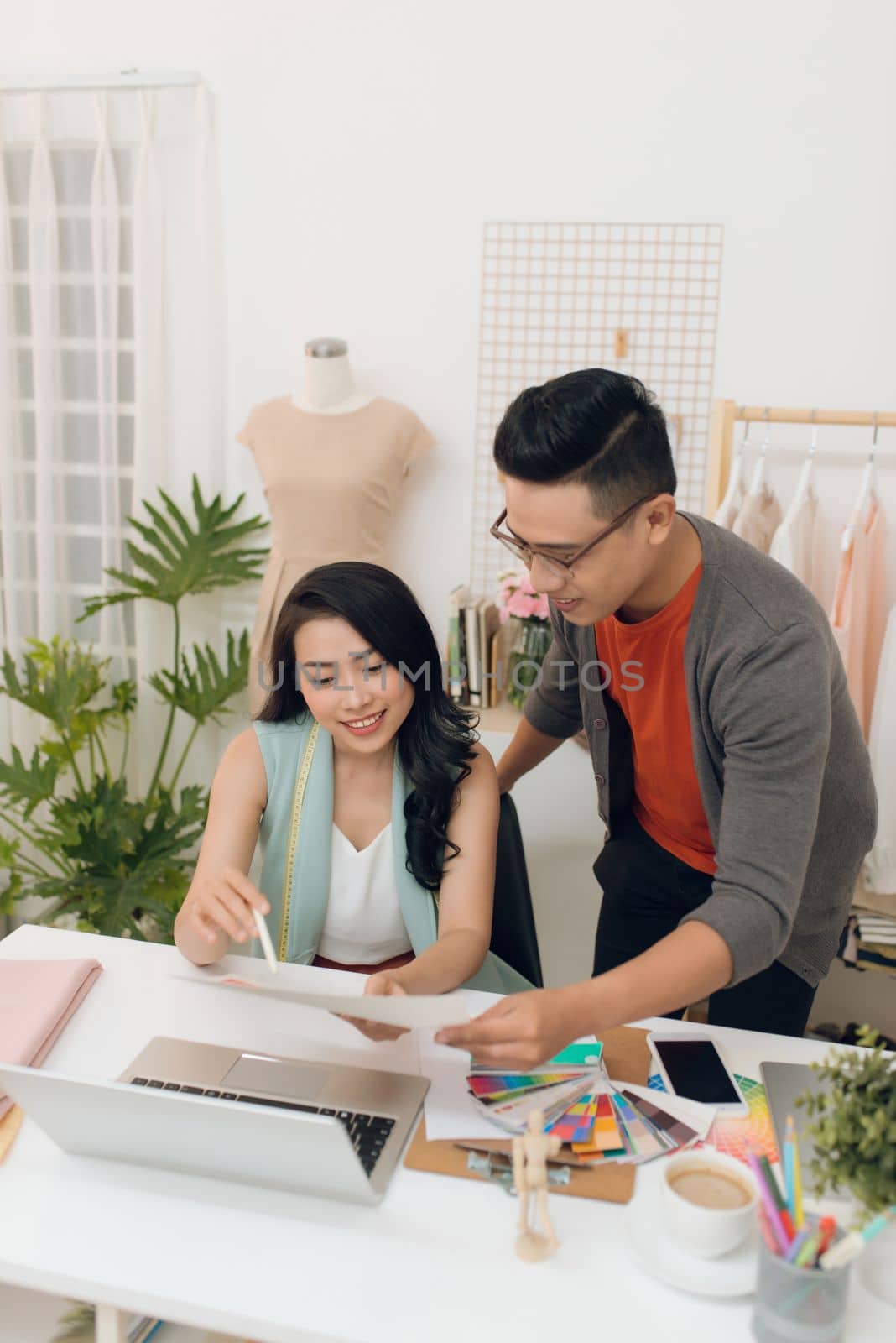 Designers team discussing fashion sketches, focused man and woman collaborating on new clothes collection creation choosing color working with swatches pantone at workplace