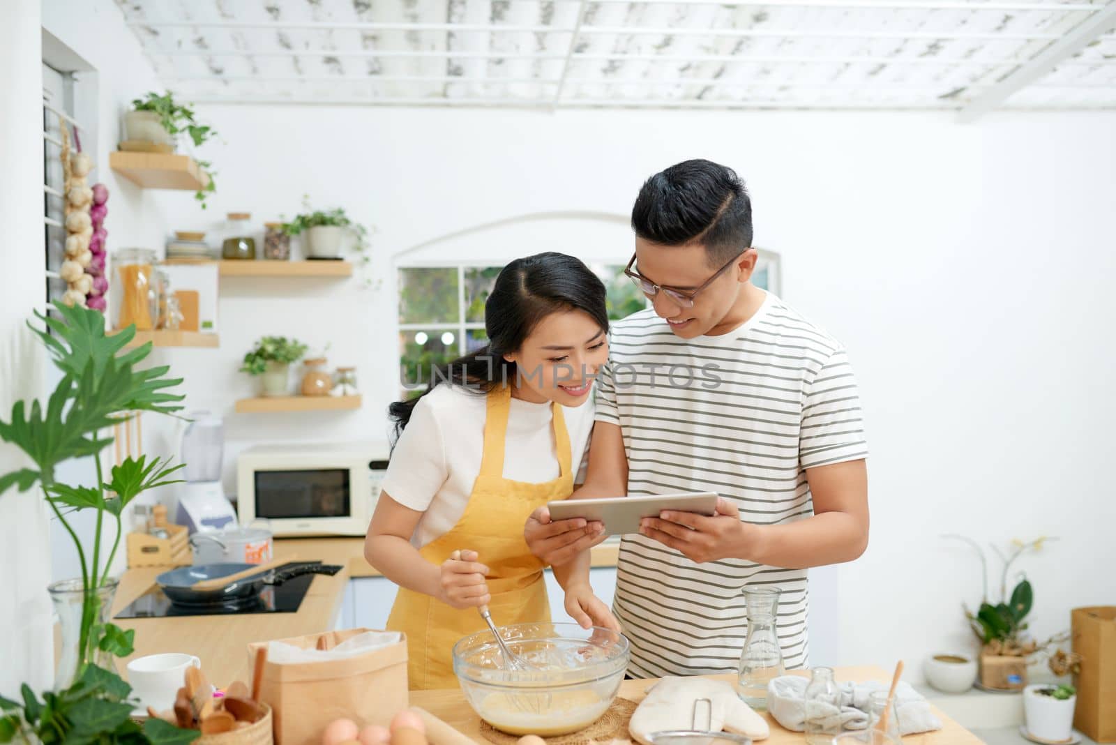 Young asian man and woman together cooking cake and bread with egg, looking menu from tablet in the flour happy relaxing in at home by makidotvn