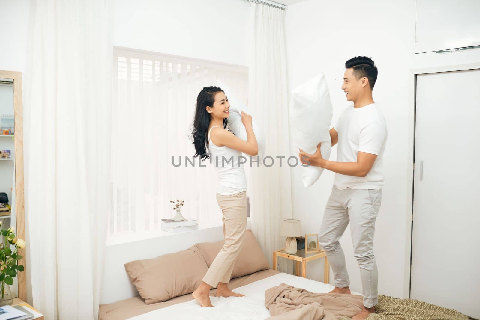 Morning of happy young couple fighting pillows in bedroom