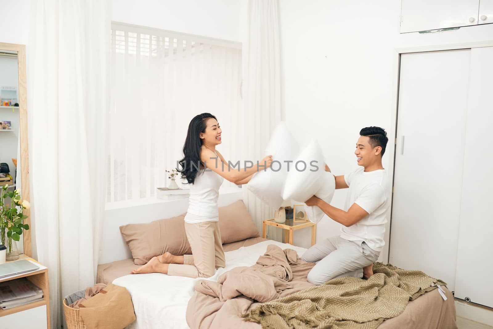 Young happy couple beat the pillows on the bed in a bedroom at home.