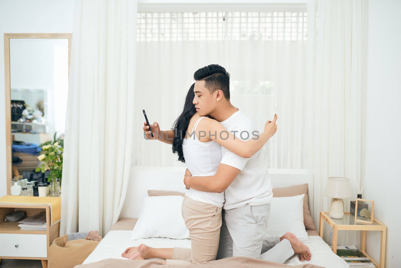 Young couple in the bedroom. Side view of unfaithful man and woman are cheating on the phone while hugging each other by makidotvn