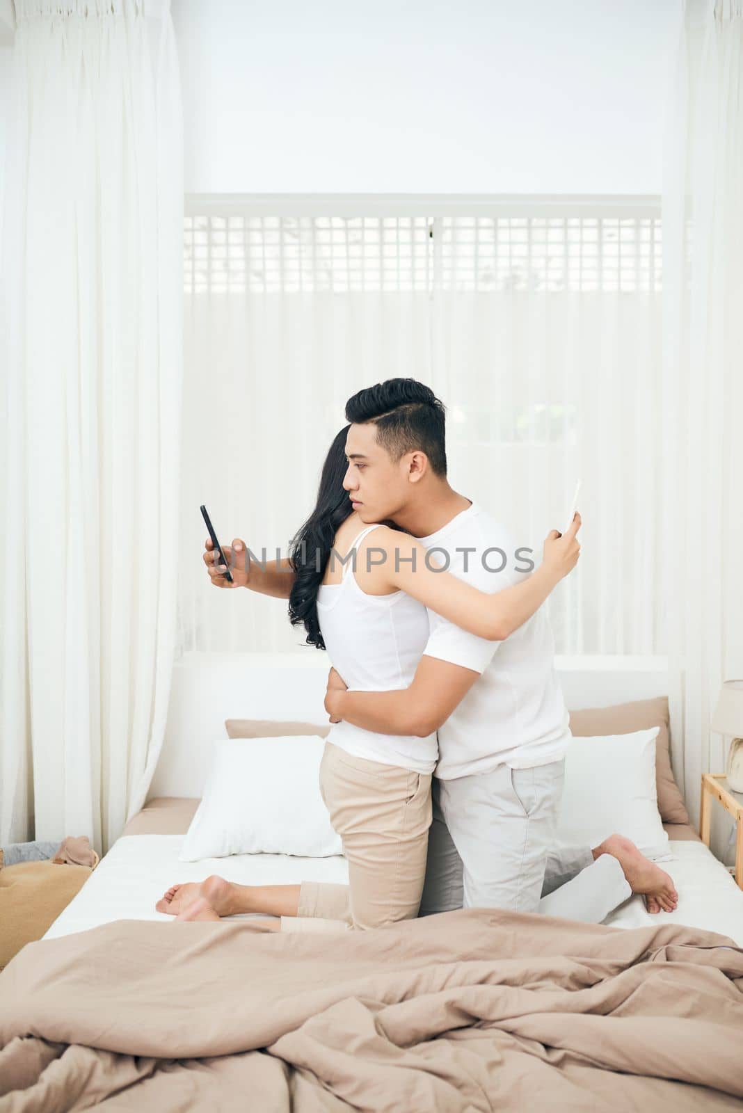 Young couple in the bedroom. Side view of unfaithful man and woman are cheating on the phone while hugging each other by makidotvn