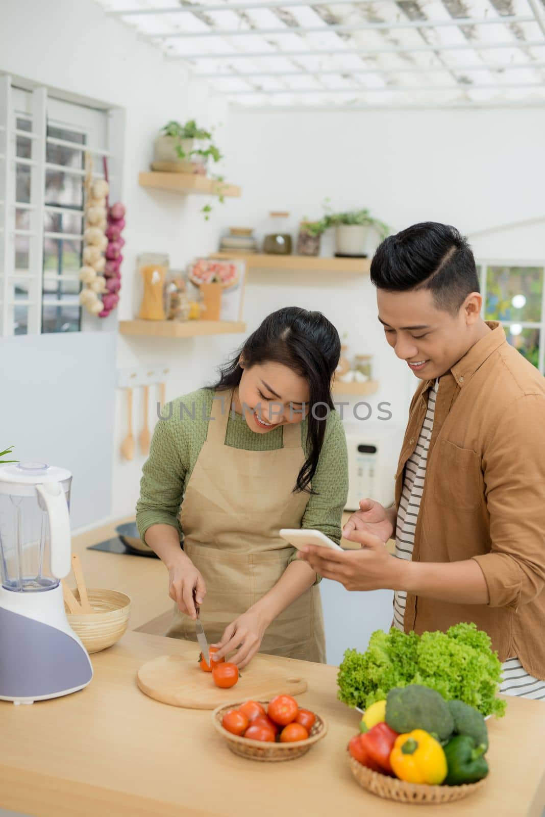 Beautiful young couple is using a cellphone and smiling while cooking in kitchen at home