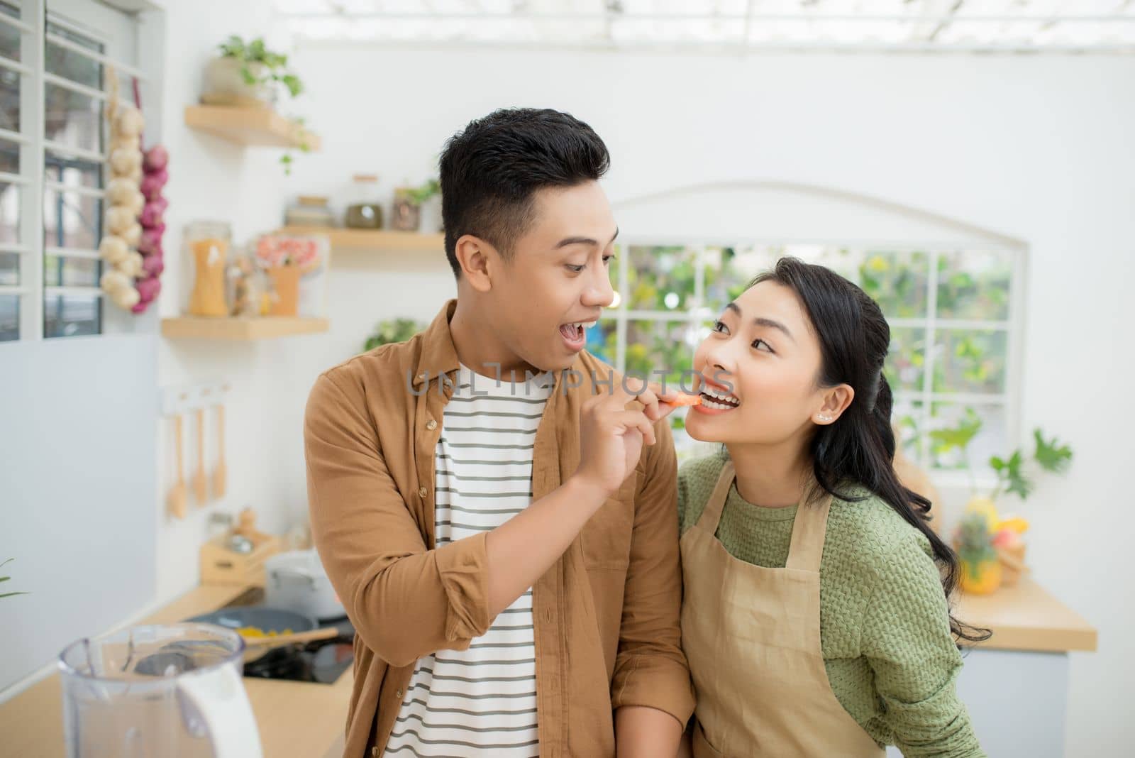 Beautiful happy asian couple are feeding each other in the kitchen.